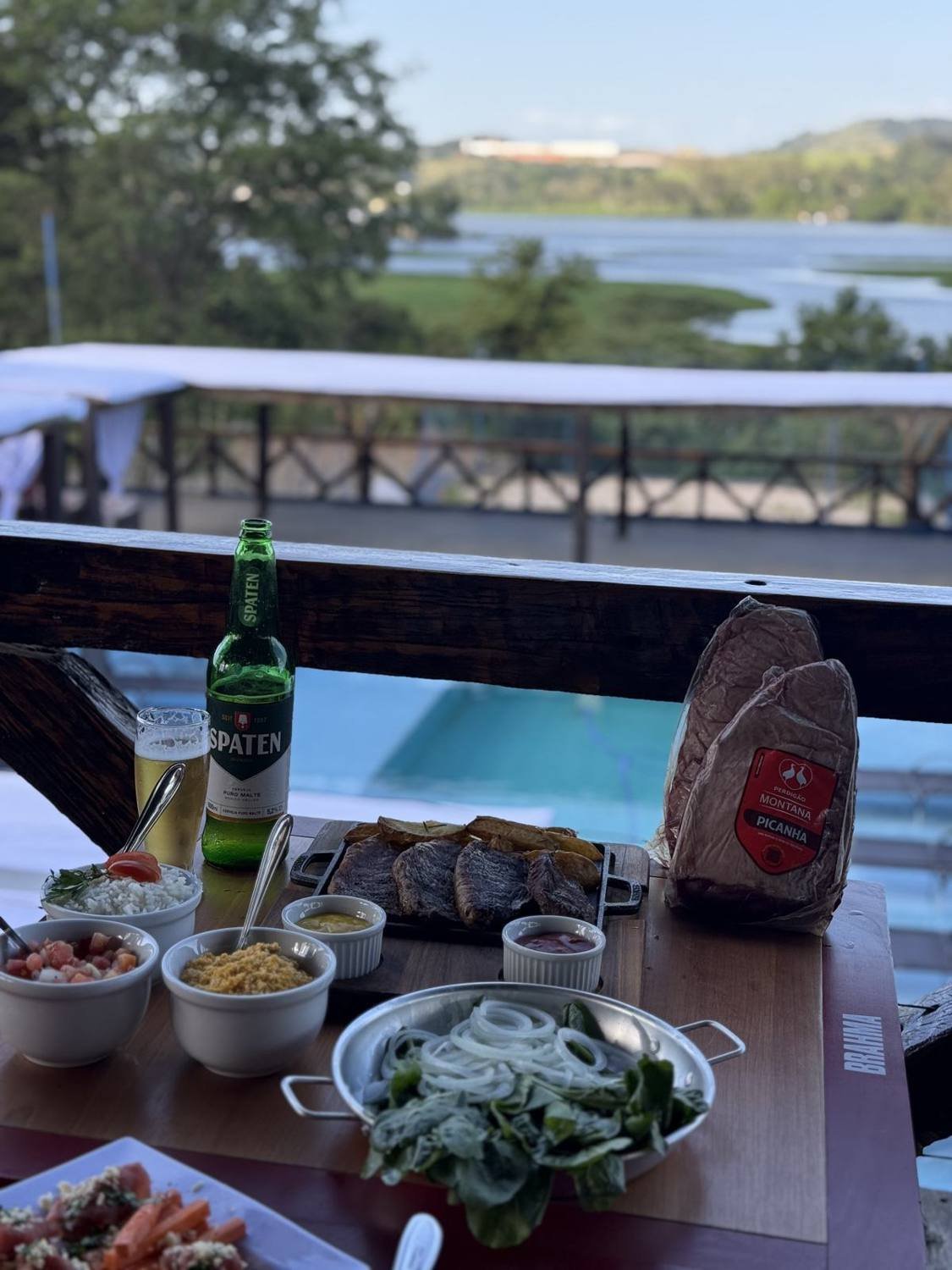 Mesa com porções, salada, cerveja e a piscina ao fundo